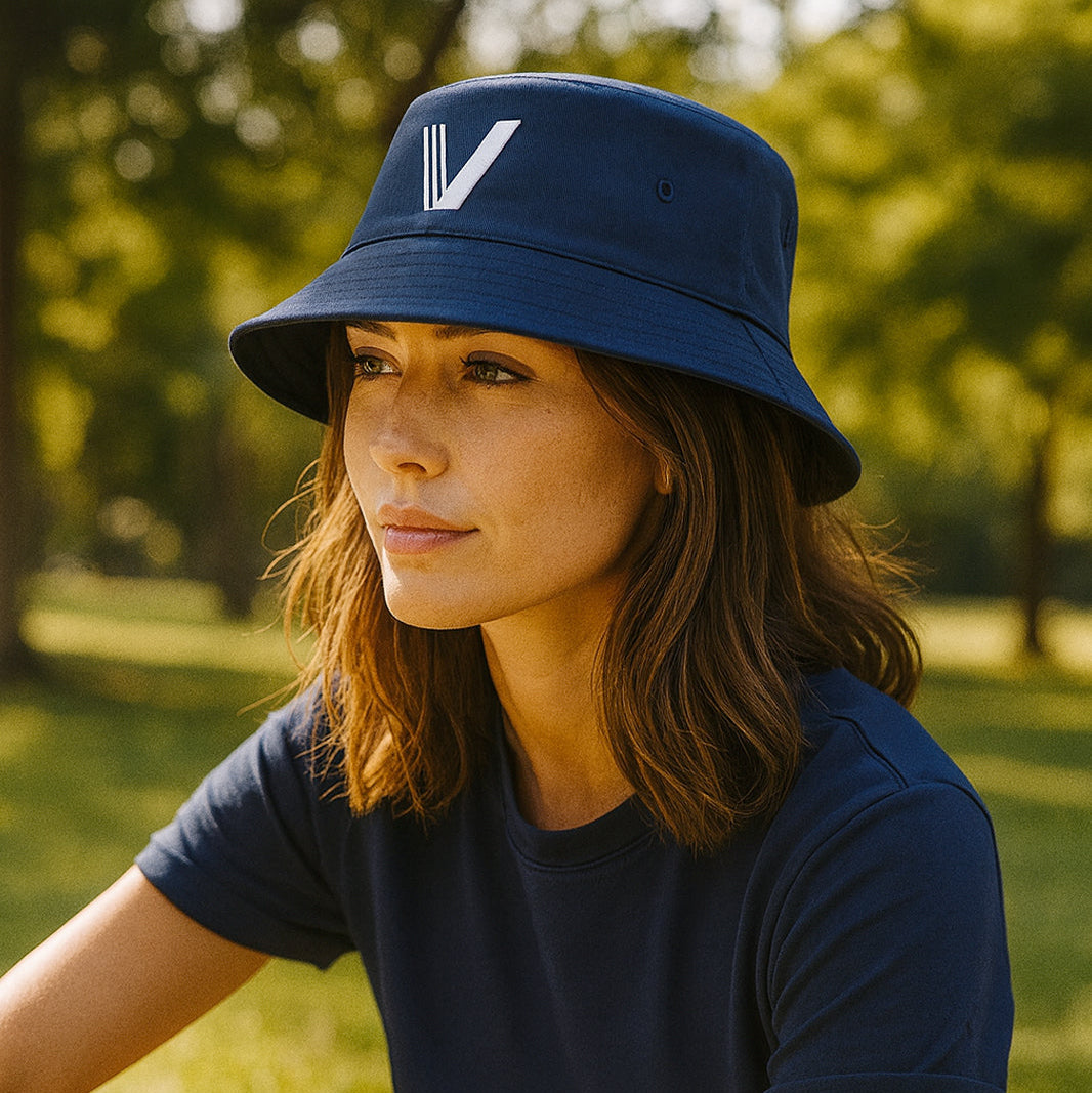 Woman wearing a navy blue bucket hat with a white V logo and a matching navy blue t-shirt outdoors.
