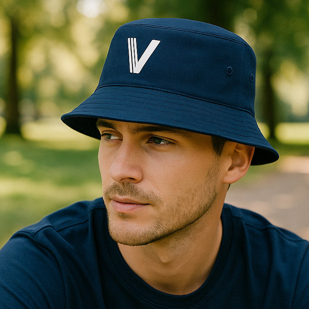 Man wearing a navy blue bucket hat with a white V logo, looking to the left in a park setting.