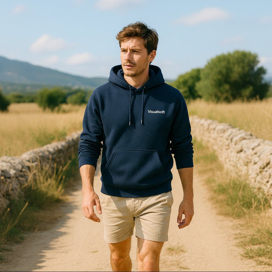 Man in a navy Visualsoft hoodie and beige shorts walks on a dirt path next to a stone wall.