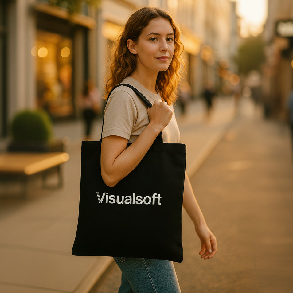 Woman with curly hair carrying a black tote bag with Visualsoft logo on a sunny street.